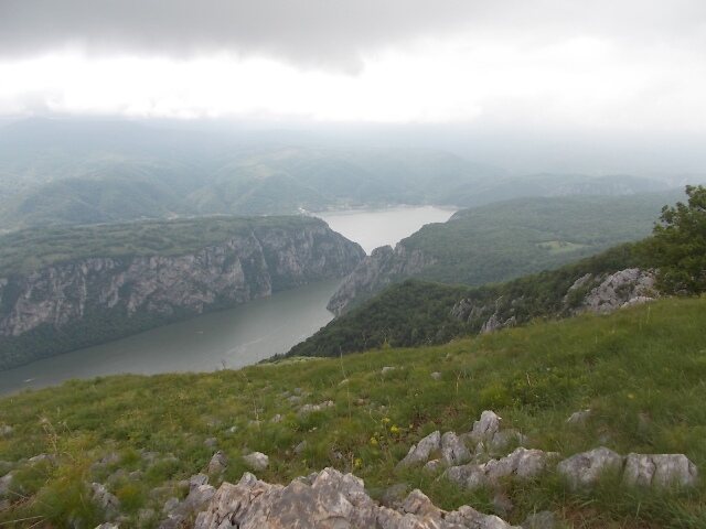 Pogled sa travnatog vrha na Dunav i okolne planine pod niskim oblacima