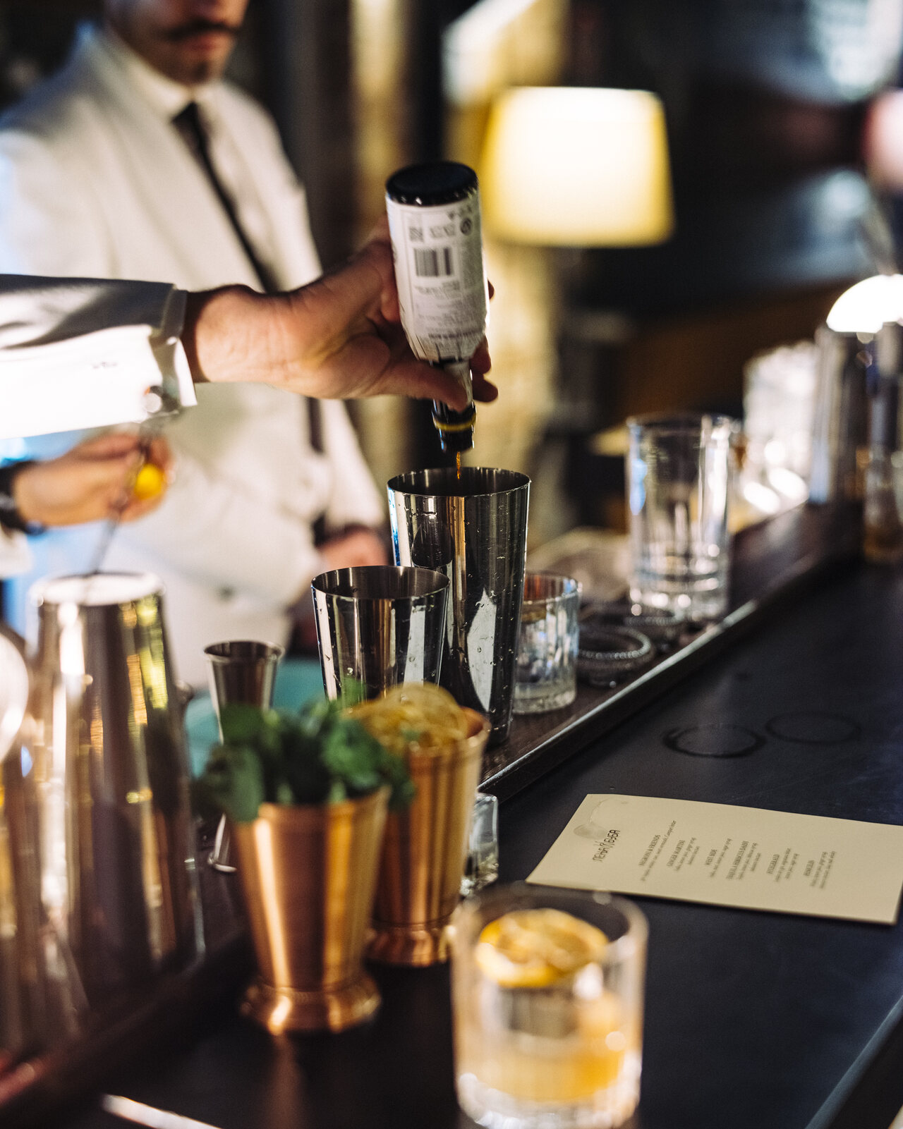 Barmen u belom sakou priprema koktel u bakarnim čašama